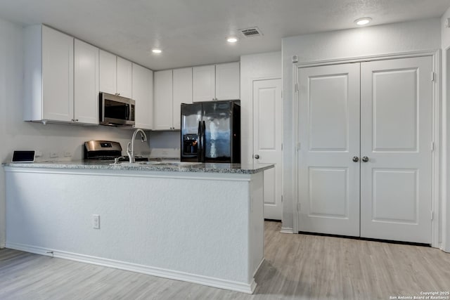 kitchen with light stone countertops, white cabinetry, appliances with stainless steel finishes, and light wood-type flooring