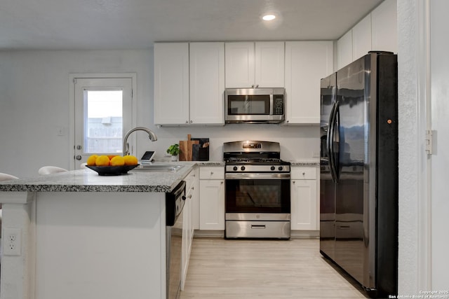 kitchen featuring sink, white cabinetry, light wood-type flooring, appliances with stainless steel finishes, and light stone counters