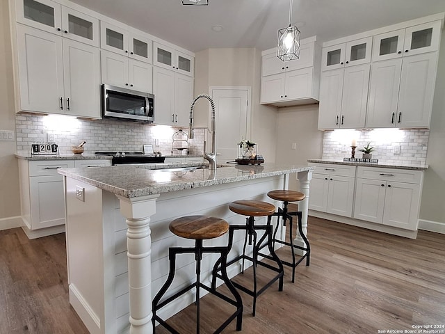 kitchen with a breakfast bar, light stone countertops, white cabinetry, and a kitchen island with sink