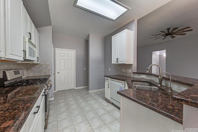 kitchen with white cabinetry, sink, kitchen peninsula, dark stone countertops, and white appliances