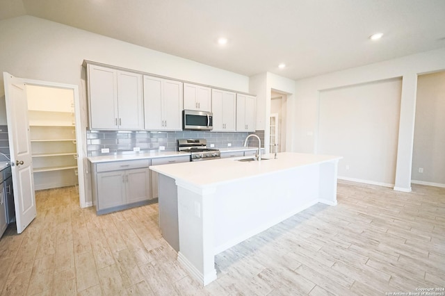 kitchen featuring sink, an island with sink, gray cabinets, decorative backsplash, and appliances with stainless steel finishes