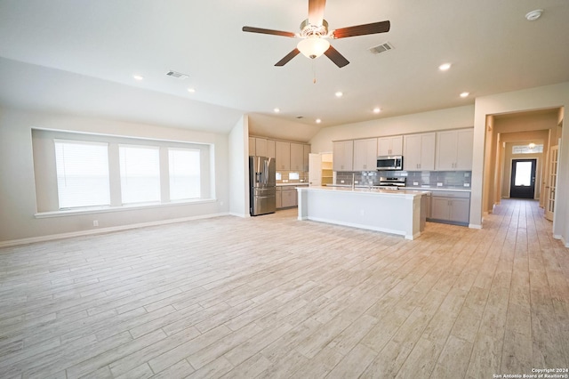 kitchen featuring light wood-type flooring, stainless steel appliances, vaulted ceiling, and an island with sink