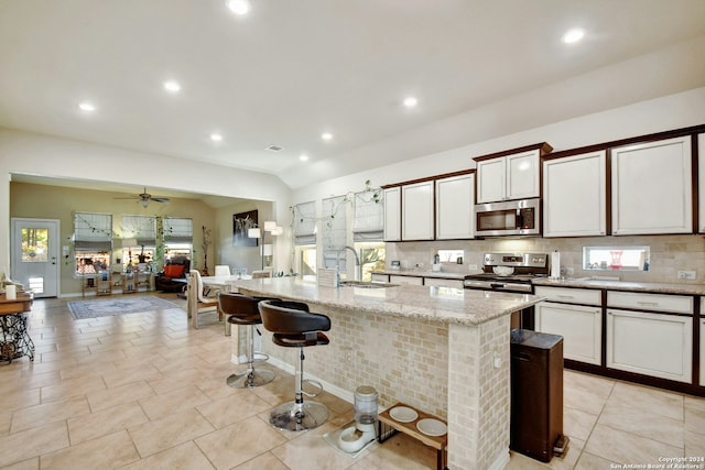 kitchen with appliances with stainless steel finishes, a breakfast bar, ceiling fan, a kitchen island with sink, and sink