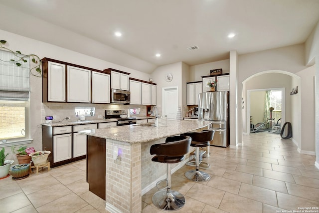 kitchen featuring a breakfast bar, a kitchen island with sink, sink, light stone counters, and stainless steel appliances