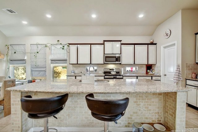 kitchen featuring backsplash, light stone counters, a breakfast bar, stainless steel appliances, and a spacious island