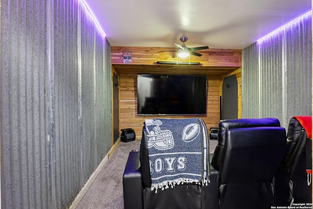 carpeted home theater room with wood walls and ceiling fan