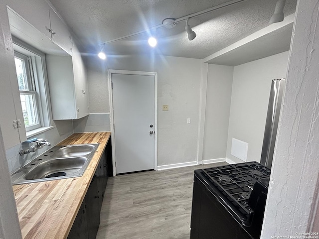 kitchen with wooden counters, track lighting, black stove, sink, and a textured ceiling