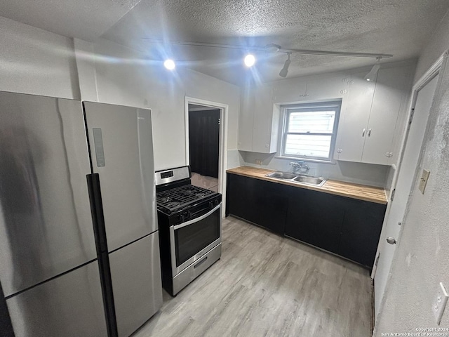 kitchen with track lighting, stainless steel appliances, sink, white cabinets, and butcher block counters