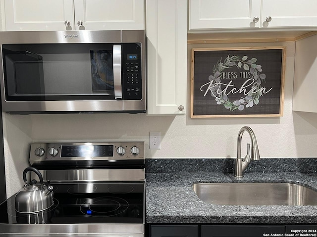 kitchen with stainless steel appliances, white cabinetry, dark stone countertops, and sink