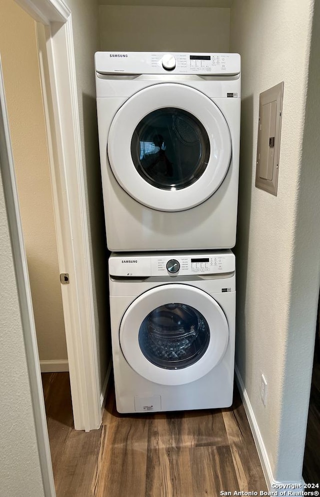 clothes washing area featuring electric panel, dark wood-type flooring, and stacked washing maching and dryer