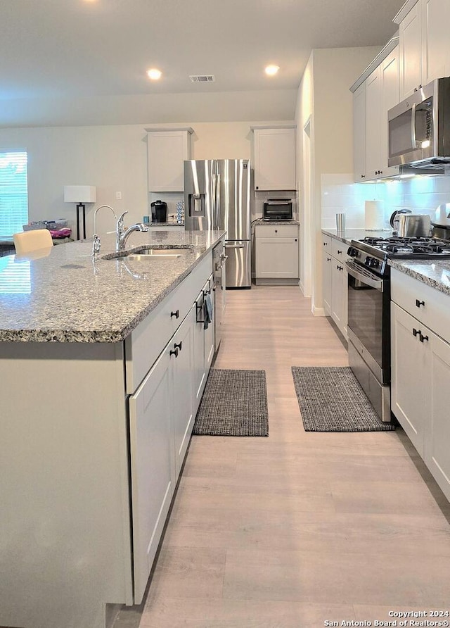 kitchen with white cabinets, sink, light wood-type flooring, an island with sink, and appliances with stainless steel finishes