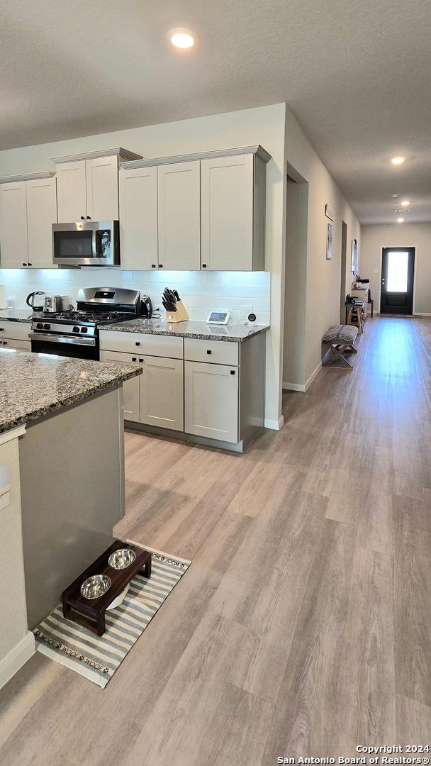 kitchen featuring decorative backsplash, light stone countertops, stainless steel appliances, and light hardwood / wood-style flooring