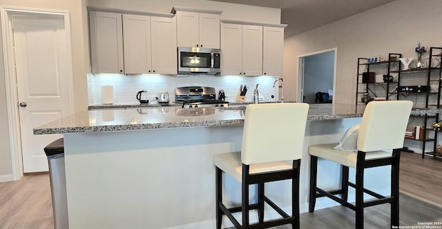 kitchen featuring a breakfast bar area, light stone countertops, stainless steel appliances, and light hardwood / wood-style floors