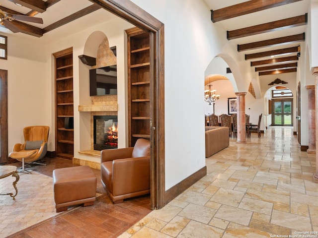 interior space with built in shelves, ceiling fan with notable chandelier, ornate columns, and beam ceiling