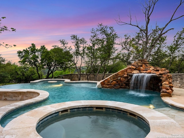 pool at dusk featuring pool water feature and an in ground hot tub