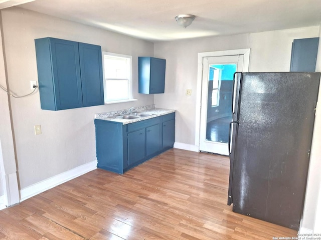 kitchen featuring black refrigerator, sink, light wood-type flooring, and blue cabinetry