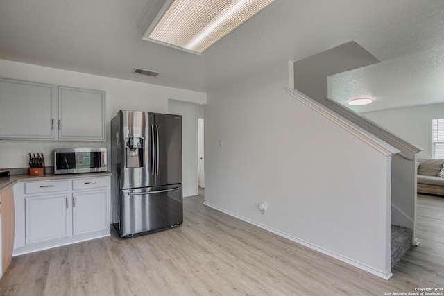 kitchen with white cabinets, light hardwood / wood-style floors, stainless steel appliances, and a textured ceiling