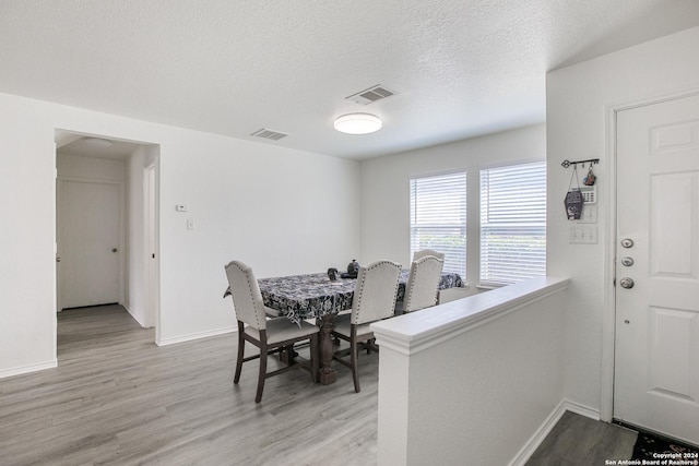 dining room with light wood-type flooring and a textured ceiling