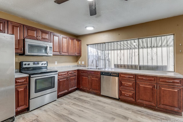 kitchen with ceiling fan, sink, stainless steel appliances, a textured ceiling, and light wood-type flooring