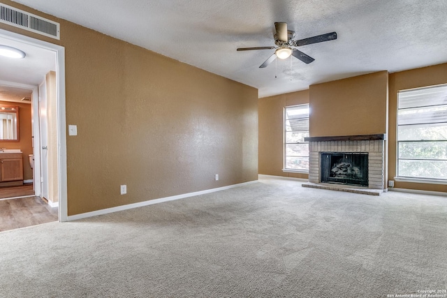 unfurnished living room with ceiling fan, carpet floors, a textured ceiling, and a brick fireplace