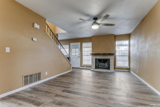 unfurnished living room with ceiling fan, a fireplace, wood-type flooring, and a textured ceiling