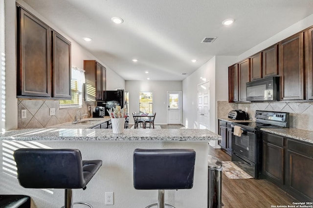 kitchen with sink, dark hardwood / wood-style flooring, kitchen peninsula, a breakfast bar area, and black appliances