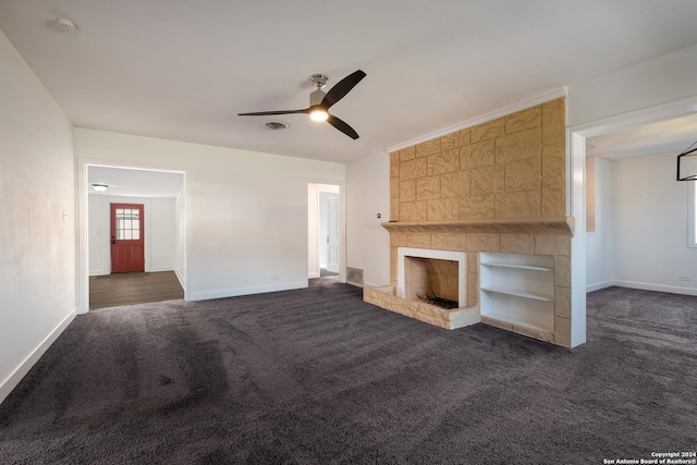 unfurnished living room featuring a large fireplace, ceiling fan, built in features, and dark carpet