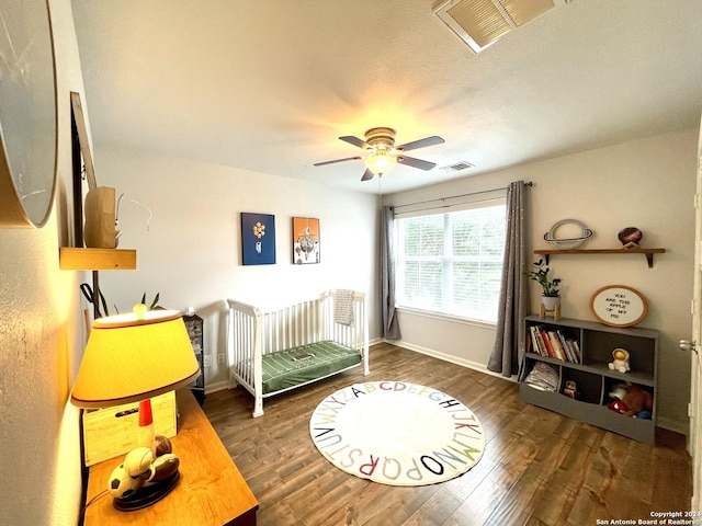 bedroom featuring a textured ceiling, ceiling fan, a crib, and dark wood-type flooring