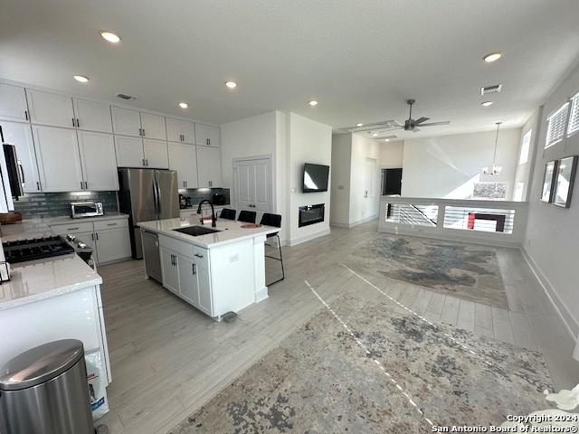 kitchen featuring appliances with stainless steel finishes, ceiling fan with notable chandelier, a kitchen island with sink, sink, and white cabinets