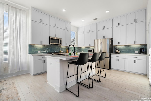 kitchen featuring white cabinetry, an island with sink, light hardwood / wood-style floors, a breakfast bar area, and appliances with stainless steel finishes