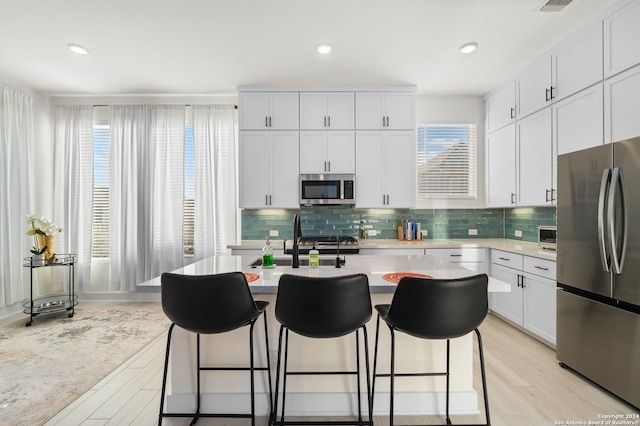 kitchen featuring white cabinetry, light stone counters, light hardwood / wood-style floors, a breakfast bar, and appliances with stainless steel finishes