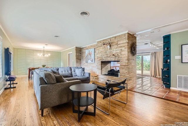 living room with an inviting chandelier, rail lighting, light hardwood / wood-style flooring, ornamental molding, and a fireplace