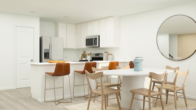 kitchen featuring white cabinets, a kitchen bar, light wood-type flooring, and stainless steel appliances