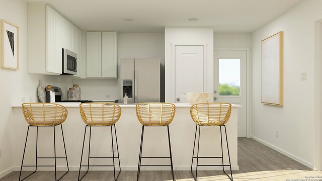 kitchen featuring light hardwood / wood-style flooring, refrigerator with ice dispenser, stove, a breakfast bar, and white cabinets