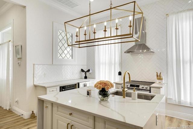 kitchen featuring decorative backsplash, pendant lighting, light stone countertops, and wall chimney range hood