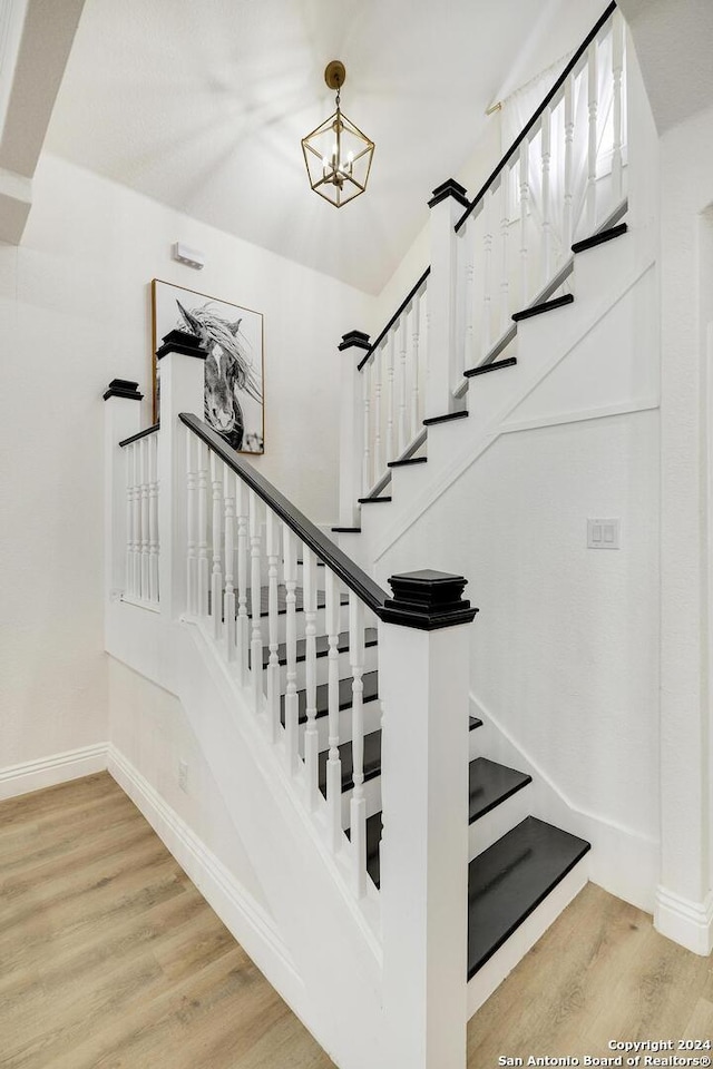 stairs featuring wood-type flooring and an inviting chandelier