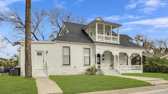 view of front of home featuring a balcony, central air condition unit, and a front lawn