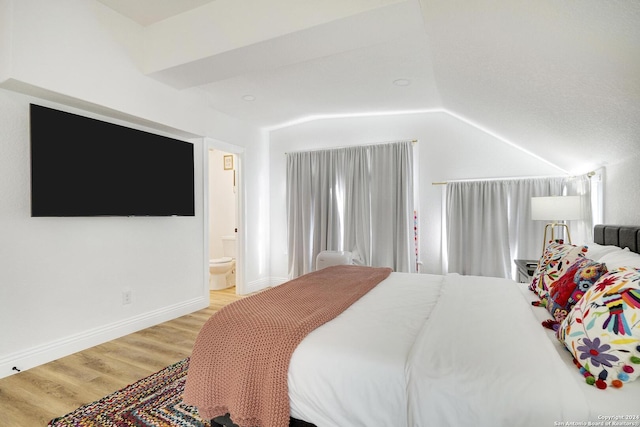 bedroom featuring ensuite bath, light wood-type flooring, and vaulted ceiling