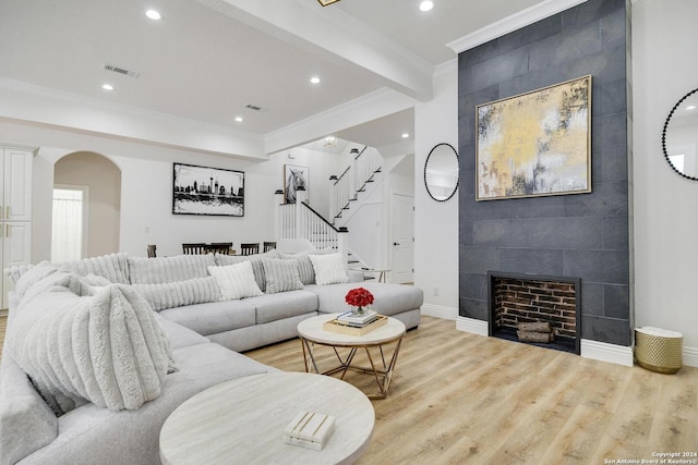 living room featuring a fireplace, light hardwood / wood-style flooring, beamed ceiling, and ornamental molding