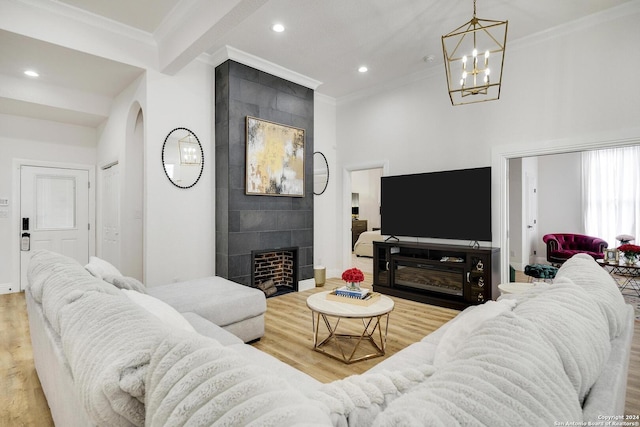 living room with a tile fireplace, light hardwood / wood-style flooring, a chandelier, and ornamental molding