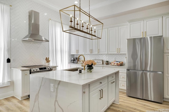 kitchen with light stone countertops, wall chimney range hood, a center island with sink, white cabinets, and appliances with stainless steel finishes