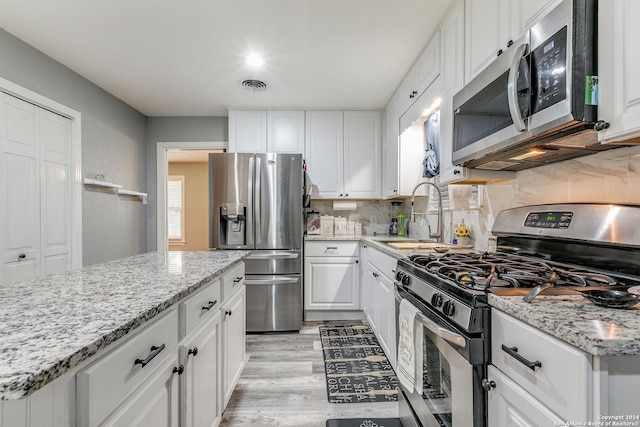 kitchen with sink, stainless steel appliances, light stone counters, decorative backsplash, and white cabinets