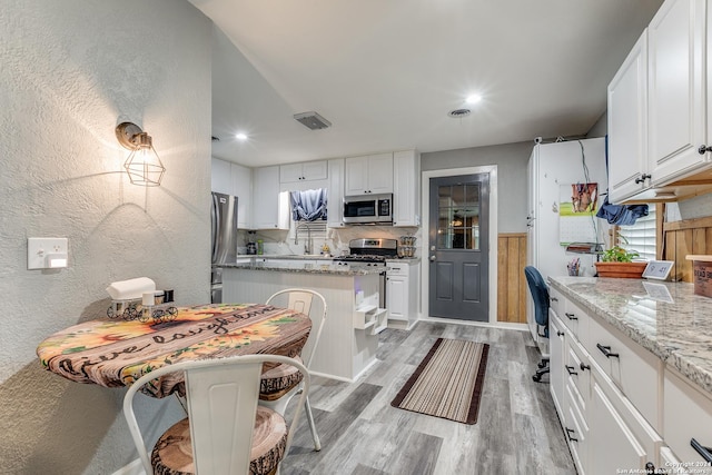 kitchen with a kitchen bar, light wood-type flooring, light stone counters, stainless steel appliances, and white cabinets