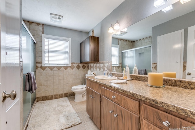 bathroom featuring vanity, tile patterned flooring, toilet, tile walls, and a shower with shower door