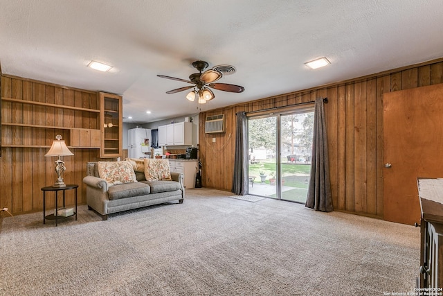 living room featuring a textured ceiling, light colored carpet, a wall mounted AC, ceiling fan, and wood walls