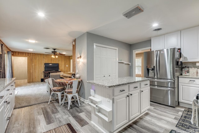 kitchen with stainless steel fridge with ice dispenser, a center island, white cabinetry, and wood walls