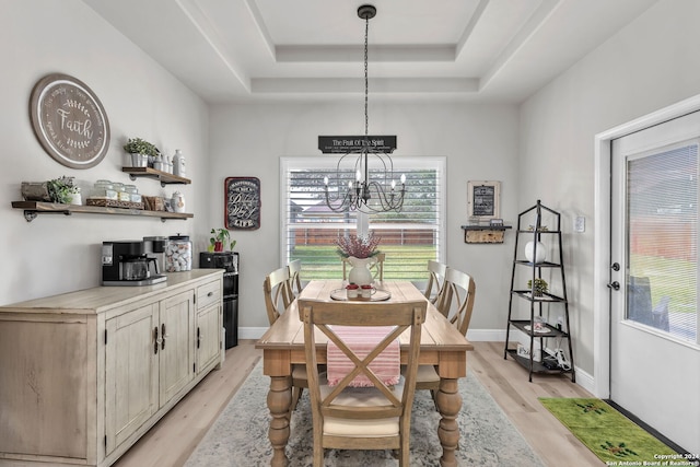 dining area with light wood-type flooring, a tray ceiling, and an inviting chandelier