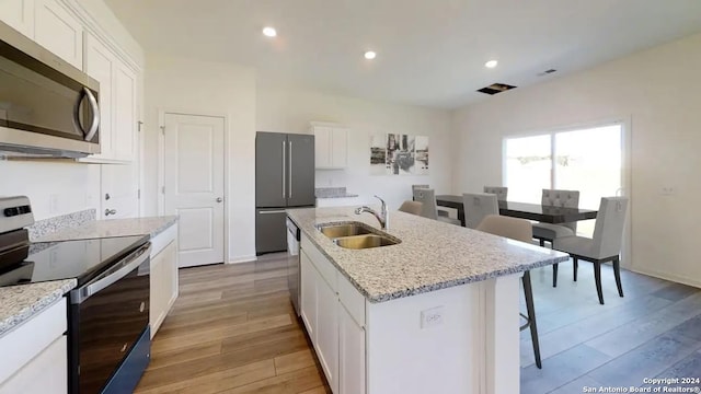 kitchen with white cabinetry, sink, stainless steel appliances, light hardwood / wood-style floors, and a kitchen island with sink