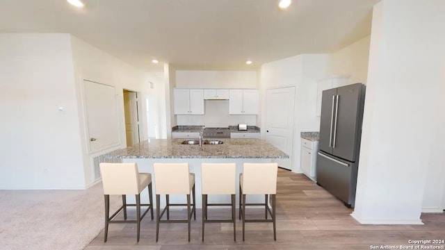 kitchen with stainless steel refrigerator, light stone countertops, a kitchen bar, a kitchen island with sink, and white cabinets