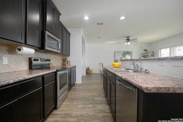 kitchen featuring stainless steel appliances, ceiling fan, sink, light hardwood / wood-style floors, and an island with sink